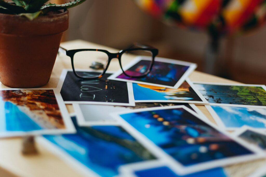 pile of colorful photos on table with glasses sitting on them